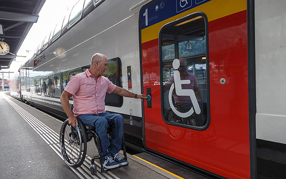 A man in a wheelchair opens the door of a train to get on.